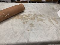 Light-colored cowhide rug laid out showing tan speckles and rolled brown leather hide on one corner.