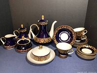 Full set displayed on blue cloth with black backdrop showing all 22 pieces including coffee pots, tea pot, creamer, sugar bowl, butter dish, cups, saucers, and plates.