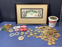 Full view of framed $3 bill with grouping of casino chips, good luck pennies, wooden nickel, and amusement park tokens on blue cloth background