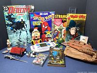 Wide shot of entire collection showing comics, handheld game, baseball glove, marbles, music cassette, and collectible figurines.