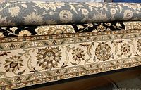 Rolled view of the wool rug showing black background and floral border pattern in brown and cream tones.