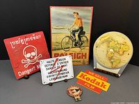 Photo of six vintage signs including international mines warning sign, high voltage German enamel sign, Kodak film sign, Raleigh bicycle sign, globe news sign, and yacht club medallion.