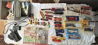 Overview of loose and boxed HO scale train cars, track pieces, and accessories laid out on a white surface showing multiple colorful cars and track sections.