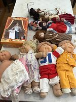 Lot overview showing the Cabbage Patch Kids dolls, porcelain Heritage Dolls, bisque sand bag dolls, and boxed Lane Bass doll.