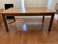 Front view of the teak extendable dining table in closed form on hardwood floor.