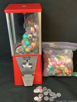 Front view of the fully assembled Oak gumball machine with colorful capsule prizes visible inside and multiple silver coins lying in front.