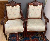 Front view of the pair of rosewood armchairs showing carved wood and floral upholstered seats and backs.