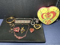 Collection of heart-themed jewelry laid out with heart-shaped tin featuring colorful design