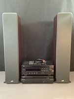 Front view of Yamaha RX-496 stereo receiver, CDC-685 CD player stacked together with front panel controls visible, placed between Polk Signature S50 tall standing speakers with gray fabric grill and wooden finish sides.