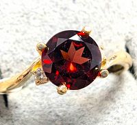 Close-up image showing the round garnet stone set in 10K yellow gold with diamond accents on the band.