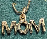 Top close-up showing the word 'MOM' on the yellow gold pendant with attached loop for chain.