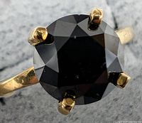 Front view of ring showing round black diamond in six-prong yellow gold setting