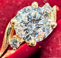 Front view of ring showing central round brilliant diamond and two side diamonds on red velvet background