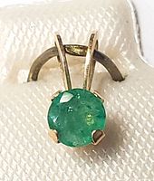 Close-up front view of 10K yellow gold emerald pendant showing the round emerald held by four prongs and the bail attachment.
