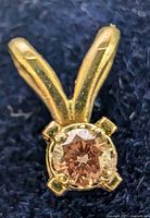 Close-up front view of 14K yellow gold pendant with a round faceted lab-created pink diamond in a four-prong setting on a dark background.