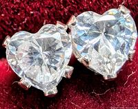 Close-up front view of the pair of heart-shaped cubic zirconia earrings set in white gold on red background.