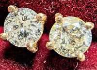 Close-up photo of round brilliant cut natural diamond stud earrings set in 14K yellow gold four-prong setting, resting on red velvet.