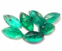 Seven marquise-cut emerald loose gemstones laid out on a white background showing color and inclusions.