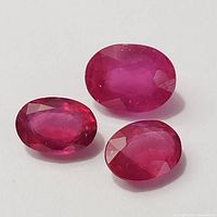 Photo showing three faceted oval enhanced ruby gemstones placed on a white surface, highlighting their color and clarity.