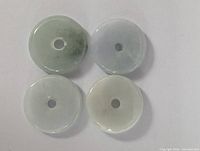 Four circular jade pendants laid flat, showing color and translucency variations with central holes.