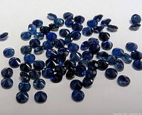 Photo displaying a collection of small round cut loose blue sapphire stones approximately 2.5 mm each on a white background.