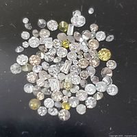 Top-down view of multiple loose diamonds of various colors and cuts on black background.