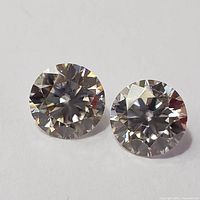 Close-up image of two loose round cut moissanite gemstones on white background, showing facet details and brilliance.