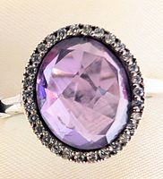 Close-up of oval faceted purple amethyst in silver ring with halo of small stones