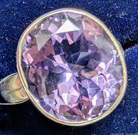 Close-up of oval faceted amethyst gemstone set in silver ring on dark blue background.