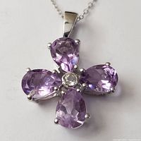 Close-up photo of the flower-shaped silver pendant with four pear-shaped amethyst stones around a central clear stone.