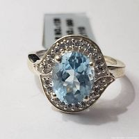 Front view of silver ring showing oval blue topaz center stone surrounded by clear accent stones in a swirl pattern