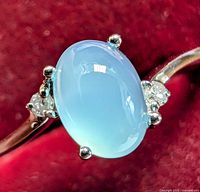 Close-up of silver ring with oval light blue chalcedony cabochon and two small natural diamonds on each side.