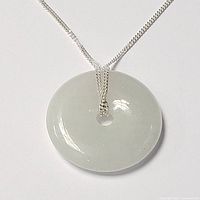 Close-up of white jade donut-shaped pendant hanging on silver chain against a white background, showing glossy and smooth surface.