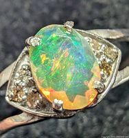 Close-up image of oval silver opal ring showing play of color in opal and diamond accents on the side.