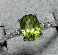 Close-up of the oval faceted green peridot gemstone in a silver band with cubic zirconia stones along the shoulders.