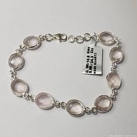 Silver rose quartz bracelet laid flat showing faceted oval stones and lobster clasp, metal tag indicating 10.8g, 24.3ct total gemstone weight, and length about 8 inches.