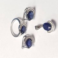 Set of one ring, two earrings, and one pendant made of sterling silver featuring dark blue oval sapphires and crescent-shaped accents with small clear stones.