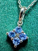 Close-up of the tanzanite pendant showing four round blue-violet stones set in silver prongs with a silver bead in the center. The pendant is against a green fabric background.