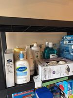 Photo showing various skincare products and slippers on a black shelf including Cetaphil cleanser, Dove body wash, Vaseline lotion, and a box of slippers.