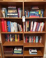 Books on a wooden bookshelf arranged vertically and horizontally, a variety of titles visible including 'The Knitting Answer Book', 'Notes from the Kitchen', and 'The Complete Knots Book'.