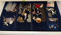 Wide view of assorted costume jewelry including earrings, necklaces, bracelets, and rings arranged on a dark fabric.