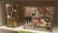Two glass and brass display cases side-by-side containing assorted animal and bird figurines, including a house figurine in one case.
