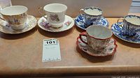 Five assorted fine china tea cups and saucers displayed on a table with a lot number card