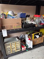Wide view of two-tier black shelving unit filled with assorted hardware supplies including masks, nuts, bolts, power charger, small containers of screws and nails on top and bottom shelves