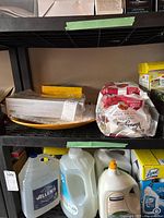 Shelf with disposable plastic dishes and serviettes with yellow large platter and bagged items