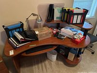 Full overview of desk with office lamps, file organizers, binders, copy paper, calculator, and assorted office supplies on top.