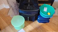 Photo showing black thermal picnic bag, 4 translucent plastic cups, 3 plastic bowls in green and blue, and light green container.