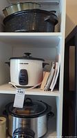 White Black+Decker rice cooker with lid on shelf, Crock-Pot slow cooker beneath, speckled roaster pan on upper shelf