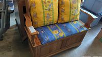 Front view of wooden storage bench showing floral cushions, carved armrests, and storage compartment under seat.