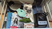 Top view showing contents of drawer with waffle makers, cookbooks, measuring spoons, blender base.
